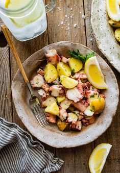 a bowl filled with potatoes and lemons next to a glass of water on top of a wooden table