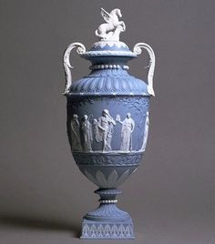 a blue vase with figures on it sitting on top of a gray table next to a white wall