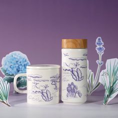 two coffee mugs sitting next to each other on a table with blue flowers in the background