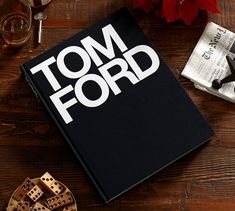 a tom ford book on a wooden table next to some wine glasses and other items