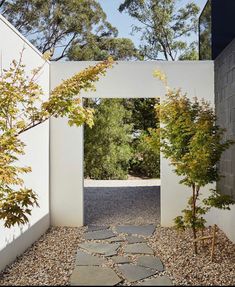 an entrance to a house with stone walkways and trees in the foreground, surrounded by white walls