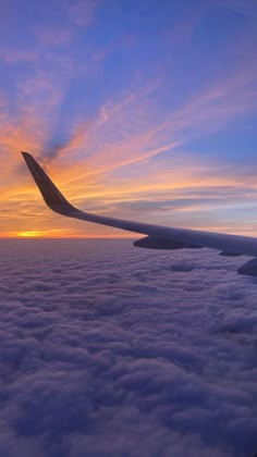 the wing of an airplane as it flies above the clouds at sunset or dawn in the sky