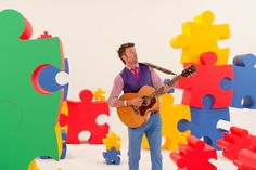 a man with a guitar standing in front of puzzle pieces