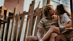 a young man and woman sitting on a wooden bench next to each other with their eyes closed