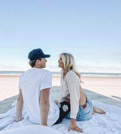 a man and woman are sitting on the beach looking at each other as they talk