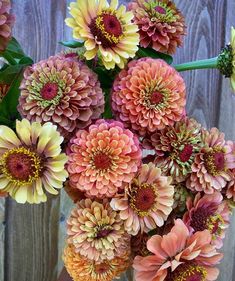 a bunch of flowers that are sitting on a wooden table in front of a fence