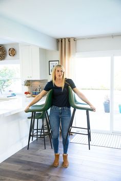 a woman standing in the middle of a kitchen with two stools on each side