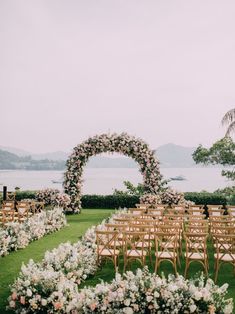 an outdoor ceremony setup with chairs and flowers on the lawn, overlooking the water in the background