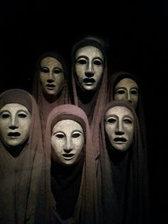 seven masks are lined up in a row on display at the museum, all wearing headscarves