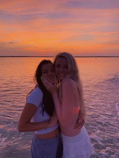 two women standing next to each other in the water at sunset on a boat ride