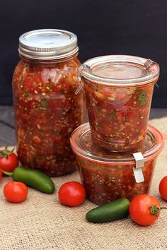 three jars filled with different kinds of food on top of a table next to tomatoes and peppers