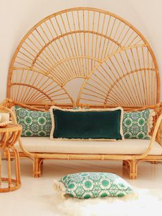 a wicker day bed with green and white pillows on the top, next to two side tables