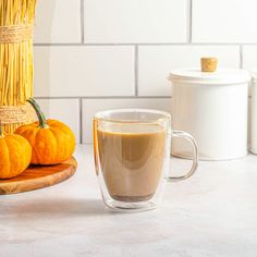 a cup of coffee sitting on top of a counter next to some pumpkins and a basket