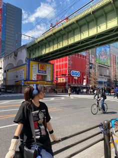 a woman with headphones is sitting on a railing in front of a city street