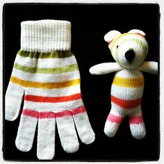 two knitted mittens and a stuffed bear are shown in this photo, one is white with multi - colored stripes