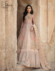 a woman standing in front of a stone wall wearing a beige and pink lehenga