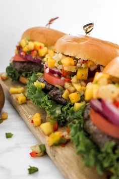 three hamburgers with lettuce, tomato and corn on them sitting on a cutting board