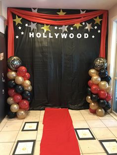 an entrance to hollywood themed party with red carpet and black backdrop, balloons and stars