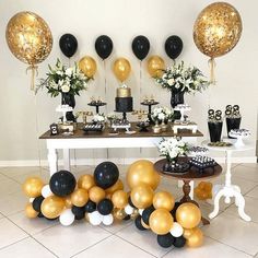 a table topped with black and gold balloons next to a white table filled with cake