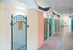 an empty hallway with green gates leading to the rooms that are painted pink, yellow and blue