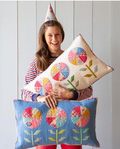 a woman is holding two pillows with flowers on them and a birthday hat on her head