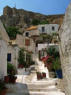 an alley way with potted plants and buildings on the hillside in front of it