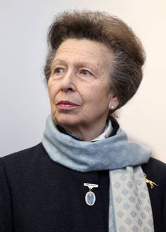 an older woman wearing a blue scarf and black jacket with a white diamond brooch on her neck