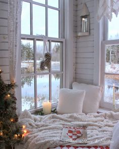 a bed with white blankets and pillows in front of a window next to a christmas tree