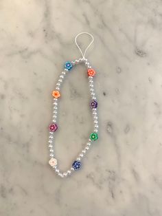 a white beaded necklace with multicolored beads and silver findings on a marble surface