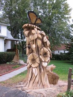 a wooden sculpture in the shape of a tree trunk with flowers and a butterfly on top