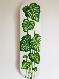 a white skateboard with green leaves painted on the front and back side, hanging on a wall