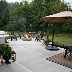 a patio with chairs and an umbrella next to a fire pit in the back yard