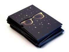 a stack of black notebooks with gold sunglasses on them and stars in the background