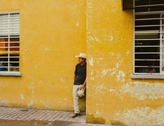 a man standing in front of a yellow building wearing a white hat and black shirt