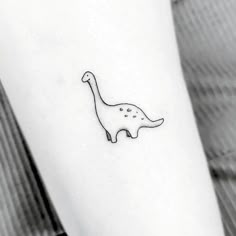 a black and white photo of a small dinosaur tattoo on the left inner arm,