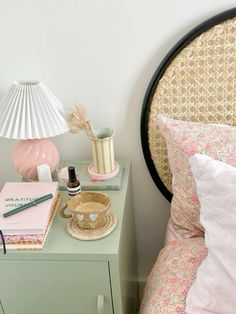 a nightstand with a lamp, notebook and other items on it next to a bed