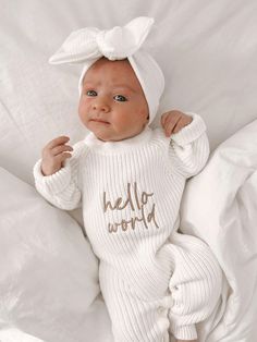 a baby wearing a white knit outfit with the word hello world on it's chest