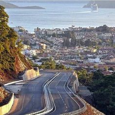 an empty road on the side of a hill with a city in the back ground