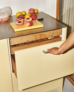 a person holding a knife in front of a drawer with apples on it and oranges