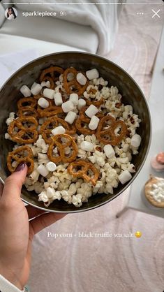 a person holding a bowl full of food with pretzels and marshmallows