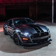 a black car parked in a garage with red lights on the side of it's headlight