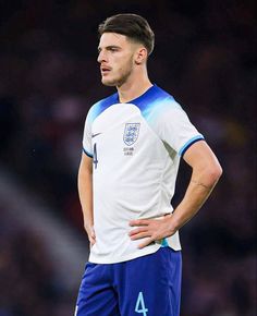 a man with his hands on his hips wearing a white and blue soccer uniform looking down