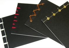 four black and gold binders are lined up on top of each other, with red pins sticking out of them