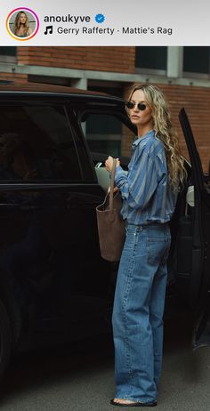 a woman standing in front of a black car with her hand on the door handle