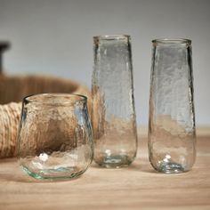 three glass vases sitting on top of a wooden table next to a wicker basket