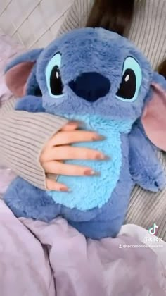 a blue stuffed animal with big eyes holding onto someone's hand while laying in bed