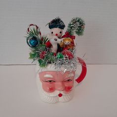 a ceramic santa claus mug with ornaments and decorations on it's head, sitting on a white surface