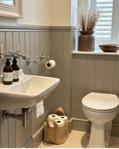 a white toilet sitting next to a sink in a bathroom under a window with shutters