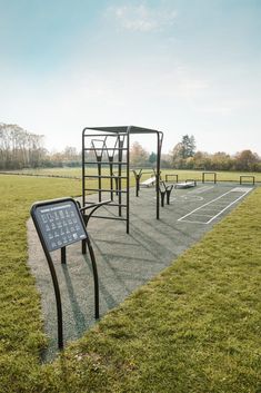 an empty playground in the middle of a grassy field with a sign on it that says,