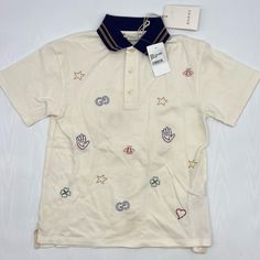 Gucci Celebrates Its Many Famous Motifs On This Polo Shirt, Embroidering The Ivory Piqu Piece With A Repeated Pattern Of Bees, Lucky Clovers, Stars, Hearts And, Of Course, The Fashion House’s Iconic ‘G’s. It’s Expertly Crafted In Italy From A Stretchy Cotton Blend And Fitted With A Contrasting, Twin-Tipped Navy Collar. 93% Cotton, 7% Elastane Piqu Fabric 2-Button Placket Made In Italy Gucci Long Sleeve Tops With Embroidered Logo, Summer Collared Tops With Embroidered Logo, Designer Embroidered Cotton Top, Gucci Cotton Tops With Embroidered Logo, Designer Embroidered Collared Tops, Casual Multicolor Gucci Tops, Cream Collared Embroidered Top, Cream Embroidered Collared Top, Casual Gucci Collared Top